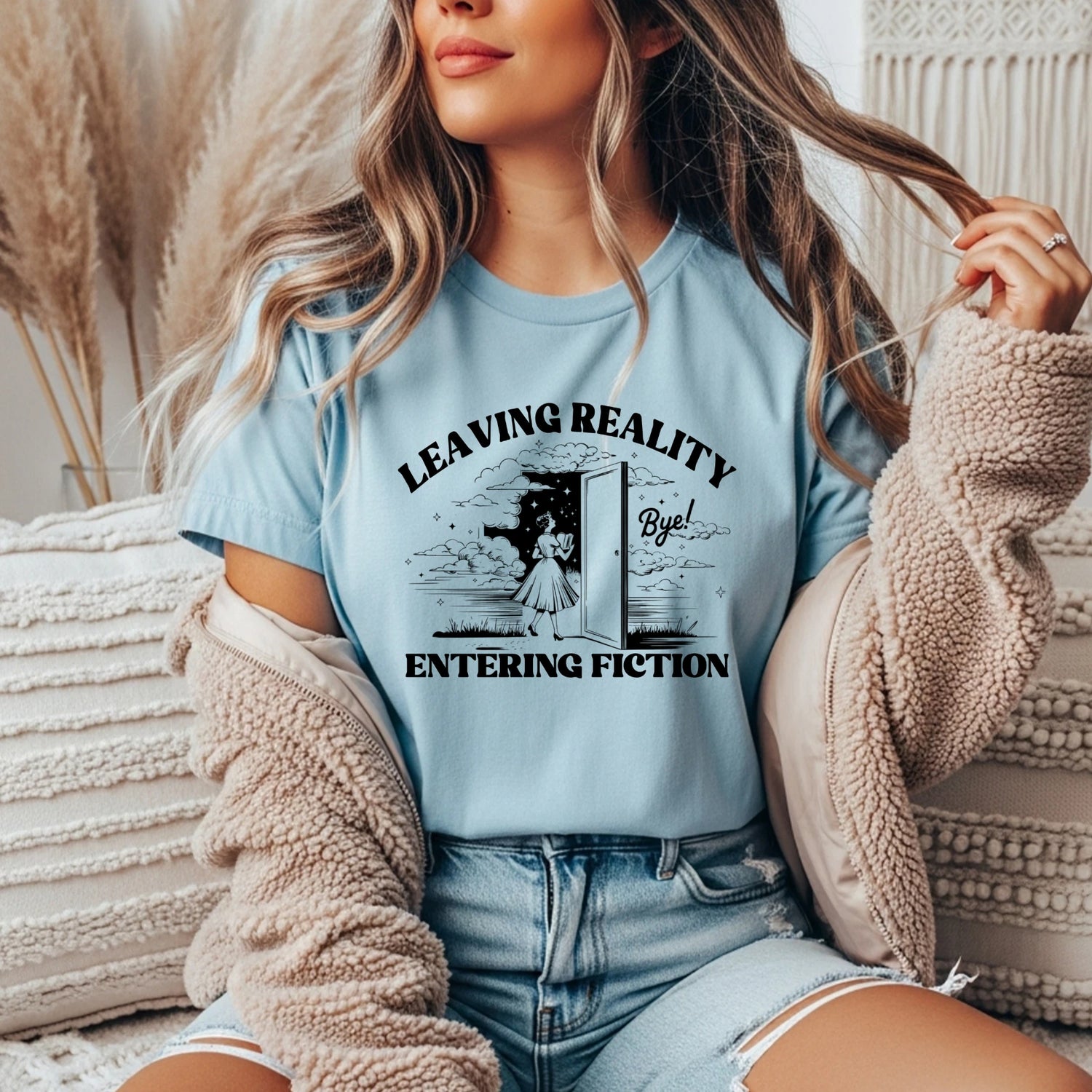 light blue tee with the phrase 'leaving reality, entering fiction' in bold bookish font